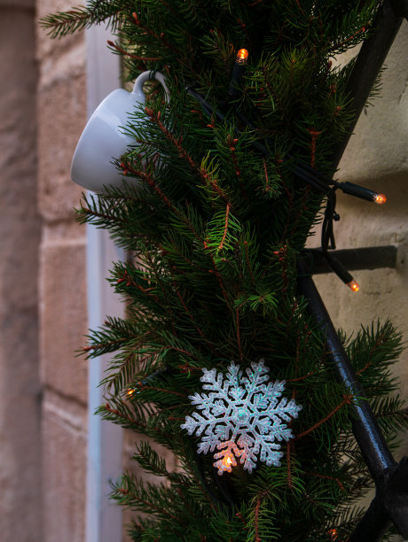 咖啡烘焙店在市中心的冬天装饰。绿色的天然冷杉树枝和白色的杯子灯在咖啡馆正面。图片下载