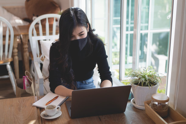 年轻女性戴着面具，工作时把笔记本电脑放在咖啡馆的木桌上，经营理念图片下载