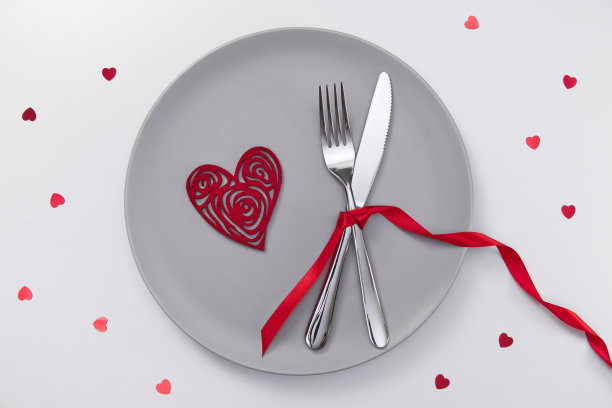 情人节的喜庆餐桌布置，平放着红心形的盘子，白桌上放着叉、刀和红丝带。爱交友的概念。放置你的文本和复制空间图片下载