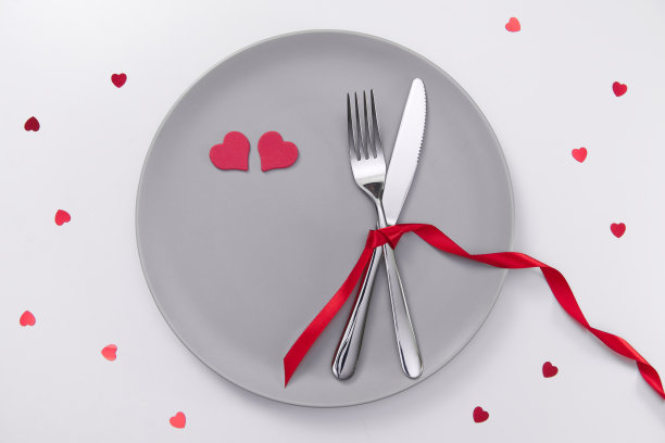 情人节的喜庆餐桌布置，平放着红心形的盘子，白桌上放着叉、刀和红丝带。爱交友的概念。放置你的文本和复制空间图片下载