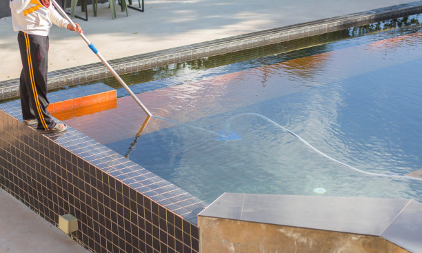 一名男子在大清早用真空管清洁器清洗游泳池图片下载