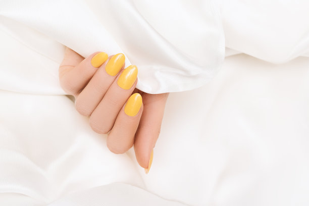 女性手与黄色指甲设计。亮黄色指甲油美甲。女人手在白色的织物背景图片下载