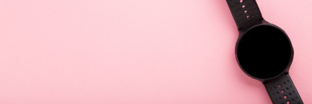 黑色智能手表在粉红色的桌子背景。柔和的颜色。查看训练信息，跑步，锻炼或其他体育活动。宽横幅。放置文本，标志或移动应用程序在空屏幕上。前视图。图片下载