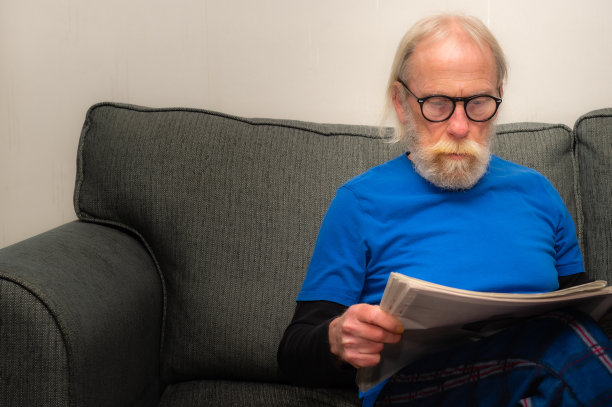 一位老人躺在沙发上，一边看报纸一边休息图片下载