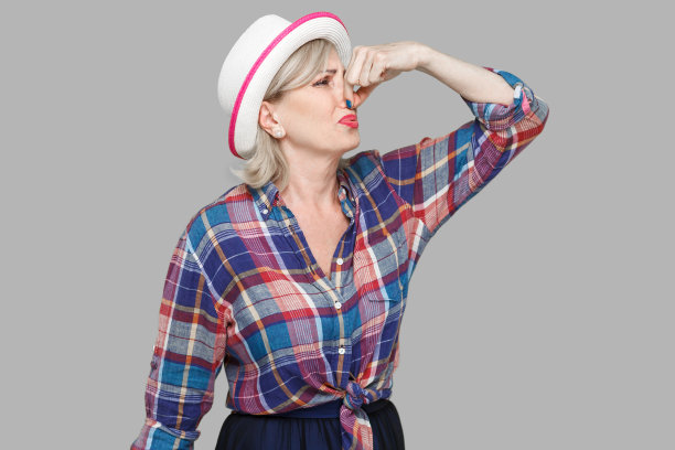 肖像厌恶现代时尚成熟的女人在休闲风格与白帽子站和捏她的鼻子，因为不好的气味感觉和忽视。图片下载