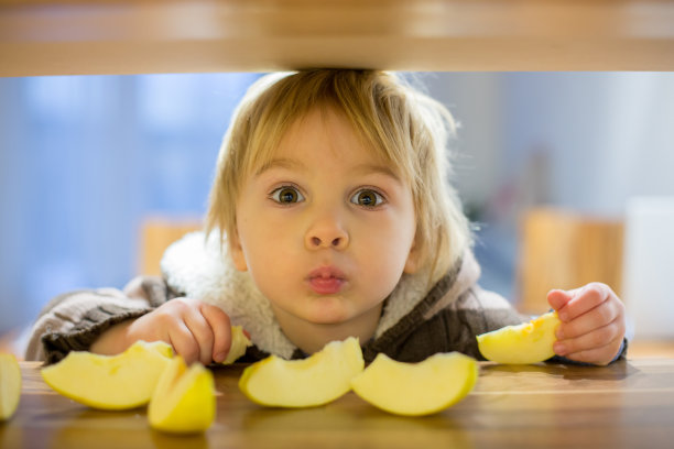 可爱的蹒跚学步的小男孩，吃着绿苹果块图片下载
