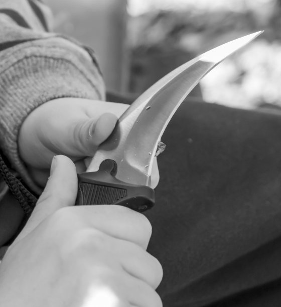 一个男孩的手正在用小刀雕刻一小块木头。男孩坐在长凳上用小刀削一块木头。黑白摄影。图片下载