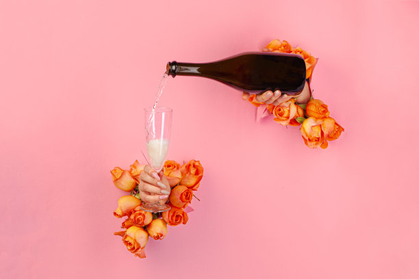 女性的手与美甲倒香槟到玻璃通过破纸上的一个洞装饰有玫瑰图片下载