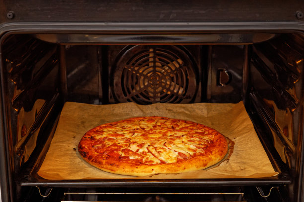 特写自制披萨与鸡肉，辣椒，番茄和奶酪在家庭烤箱。浅的焦点。图片下载