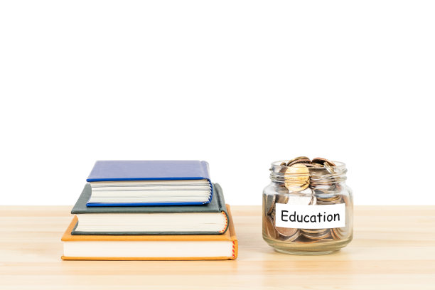 木桌上贴有标签的玻璃罐内硬币，白色背景上有书堆，为教育和奖学金节省概念图片下载