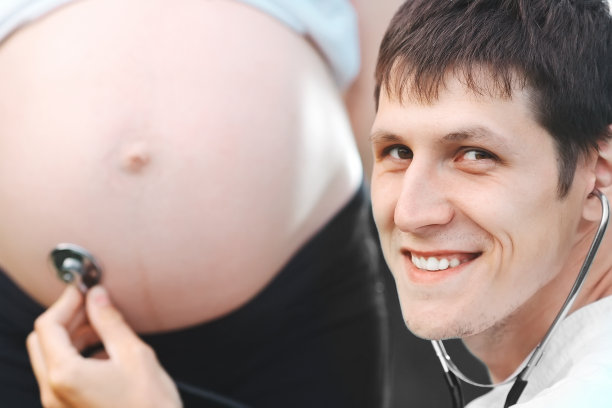 年轻的医生听着孕妇的胃，对着镜头微笑。为了有个健康的孕期图片下载