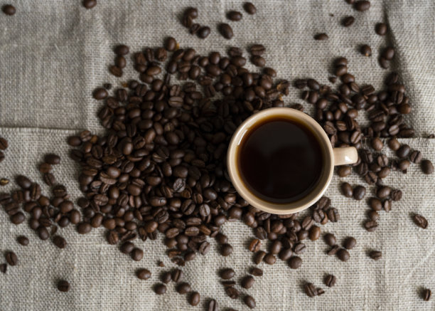 咖啡杯与烘咖啡豆亚麻的背景。一杯撒着咖啡豆的黑咖啡。新鲜的咖啡豆。图片下载