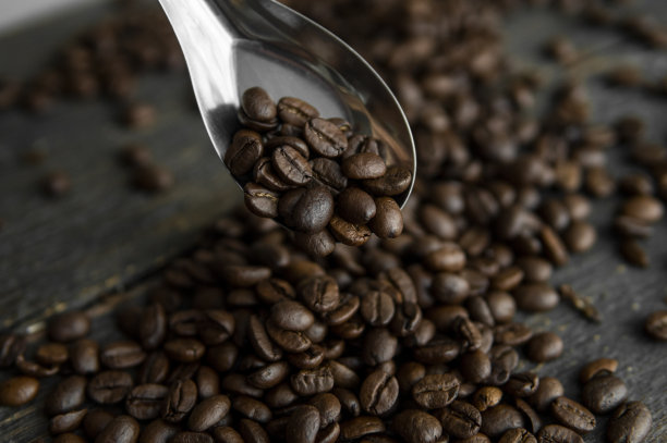 金属勺子里装着新鲜烤过的阿拉比卡咖啡豆，木桌上撒着咖啡豆。图片下载