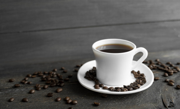 木桌背景上放着烤咖啡豆的咖啡杯。木桌上放着一杯黑咖啡和散落的咖啡豆。新鲜的咖啡豆。图片下载