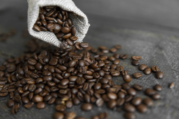 亚麻袋子里的咖啡豆散落在木桌上。新鲜烘焙的阿拉比卡咖啡豆。图片下载