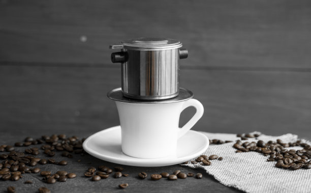 白色的咖啡杯，上面有金属过滤器，木桌上散落着咖啡豆。传统的越南咖啡。图片下载