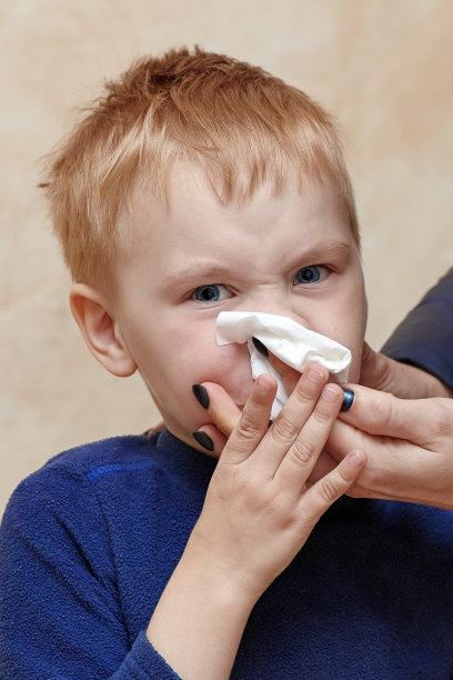 金发小男孩打喷嚏或擤鼻涕，妈妈帮他的手。眯着眼睛，皱着眉头，脸颊酥脆，可怜的病宝宝。图片下载