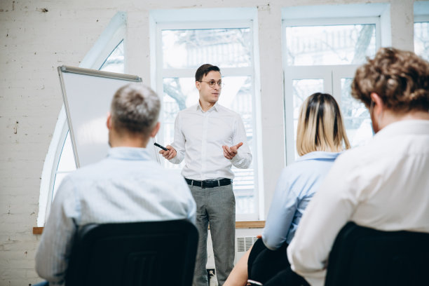 男演讲人在车间大厅演讲。观众或会议厅。未被认出的戴面罩的参与者的后视图，Covid。图片下载