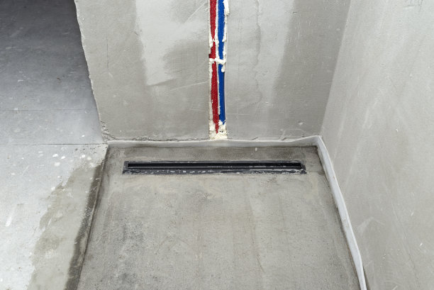 一个现代的黑色线性淋浴排水安装在淋浴地板上，可见水管在墙上。图片下载