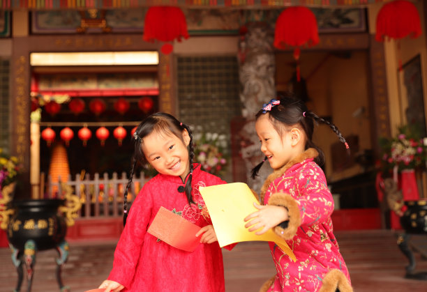两个亚洲双胞胎女孩穿着旗袍在寺庙前进行新年访问。图片下载