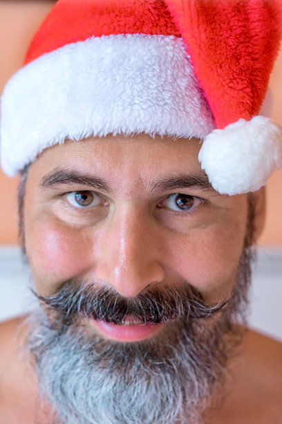 特写微笑，晒黑，蓄胡须的白种人在圣诞老人帽站在仙人掌前的海滩上。图片下载