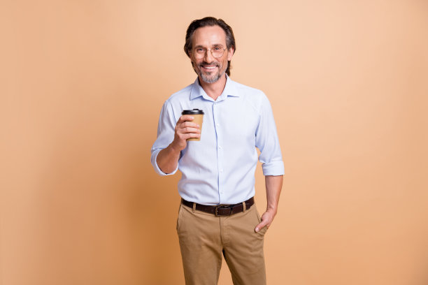 照片正面的家伙拿着外卖咖啡杯手口袋看相机戴眼镜衬衫孤立的米色背景图片下载