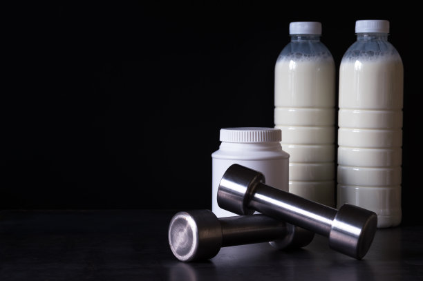 带有蛋白质粉的哑铃和奶昔瓶在黑色金属背景的塑料包装中。背景。图片下载
