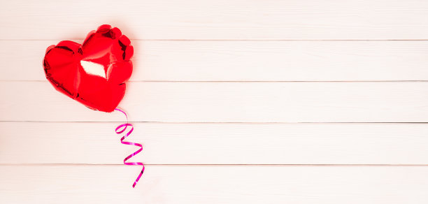 一个闪闪发光的红色心形气球，上面系着一条粉色的丝带，白色的米色和粉色的木制背景是情人节的横幅。情人节横幅。2月14日的横幅概念。带有文本位置的横幅。copyspace。平躺图片下载