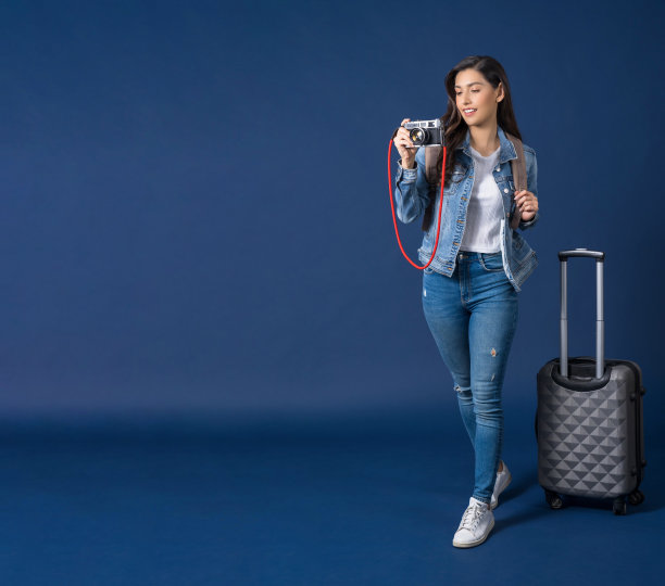快乐年轻的亚洲女人拿着和拍摄照片与蓝色背景的复古相机，携带背包客和行李，假期和旅行的概念图片下载