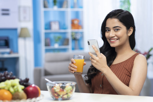 年轻女性喝着橙汁和水果，用手机上的照片图片下载
