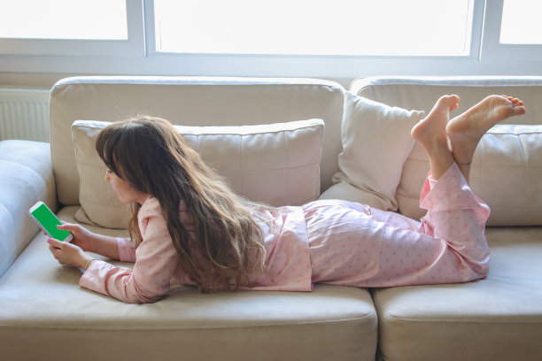 一个女人在家里的沙发上用智能手机购物。图片下载