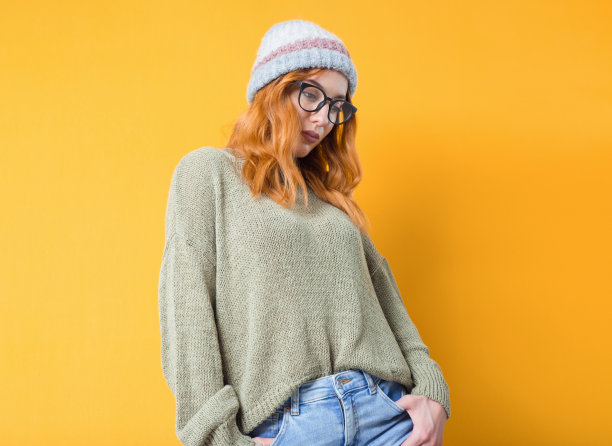 年轻女子低头看，手握口袋，站着摆姿势，孤立在黄色背景中。长得很漂亮的女孩图片下载