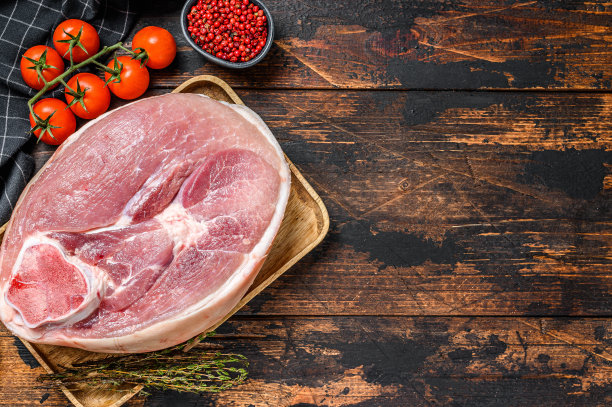 将生猪肉的指节、腿切在砧板上。农场新鲜的肉。木制的黑色背景。前视图。本空间图片下载