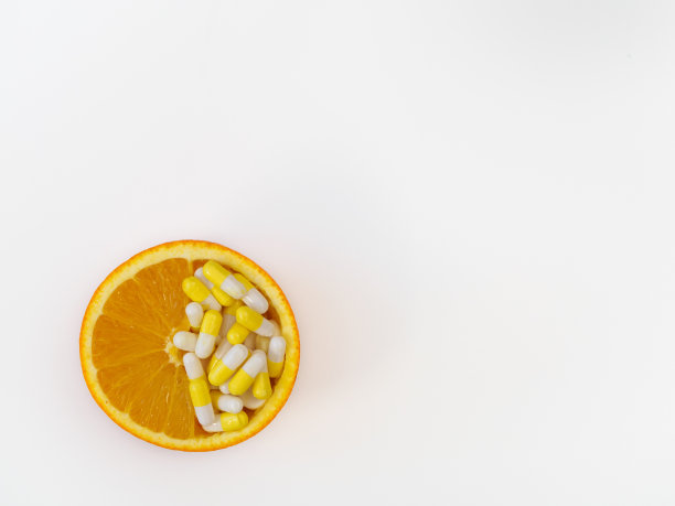 半个橙子，里面有维生素。白色背景上是橙子和维生素胶囊。健康和天然维生素的概念图片下载