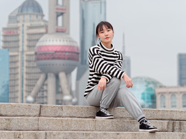 一名中国年轻女子坐在以上海地标为背景的台阶上的肖像。图片下载