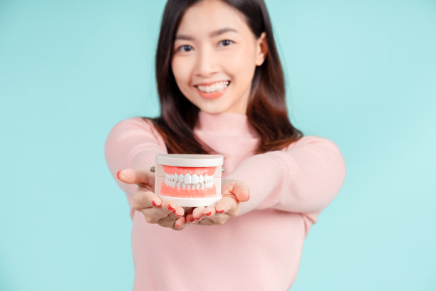 牙齿的亚洲妇女与牙齿样本和白色的牙齿增加信心为健康的蓝色背景孤立工作室拍摄，幸福的青少年微笑的面部表情。图片下载