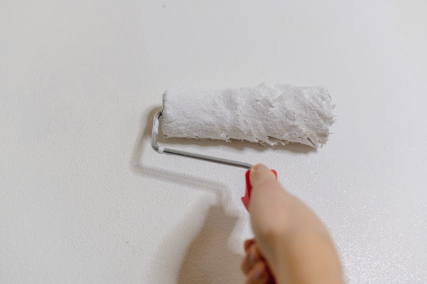 不可辨认的手握油漆辊漆与白色染料在墙上。图片下载