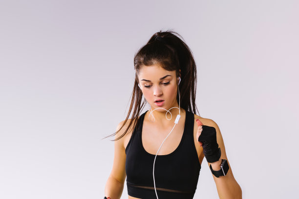 放大照片的一个黑发女孩跑步在一个黑色的顶部和耳机在耳朵。白色背景和侧面空间。图片下载