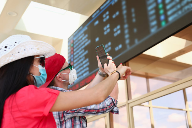 一名戴着医用防护口罩的男子和一名女子在火车站的信息板上拍照图片下载