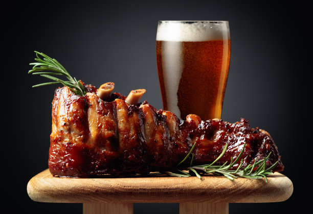 一杯啤酒和烤猪排配迷迭香放在木板上。图片下载