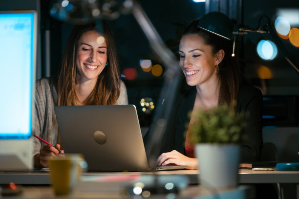 两个聪明的商业女性一起工作与笔记本电脑在办公室交谈。图片下载