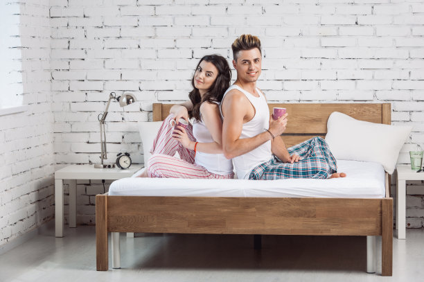 一对快乐的夫妇躺在家里的床上喝着茶图片下载