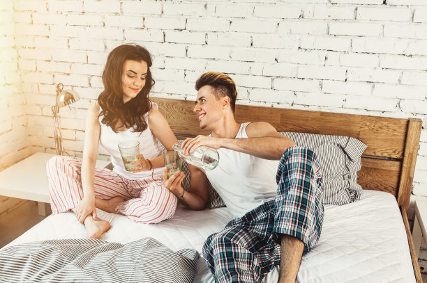 幸福的年轻夫妇穿着睡衣，在家里的床上喝着水图片下载