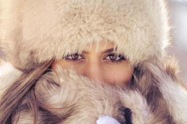 大雪纷飞的白天，在城市冬季公园里，一位戴着毛皮帽子的美女正看着镜头图片下载