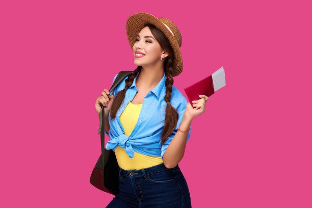 微笑的白人女学生拿着护照和机票。女孩穿着便服，戴着草帽。女性旅行者在粉红色孤立的背景。图片下载