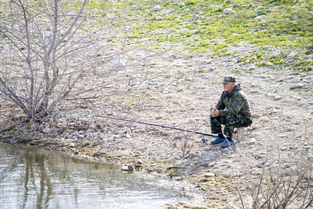 夕阳西下时，一个人独自坐在码头上，在海湾里钓鱼。图片下载