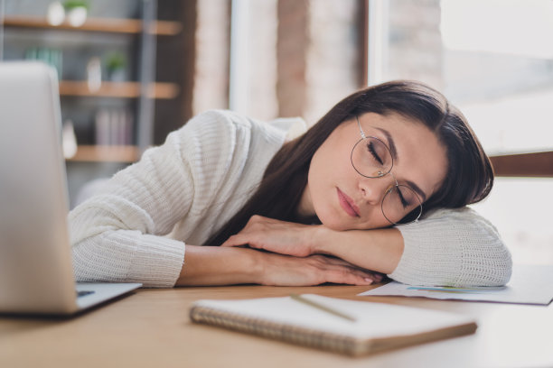 梦幻女士的照片躺桌子睡觉工作场所放松戴眼镜白色套衫在客厅在家室内图片下载