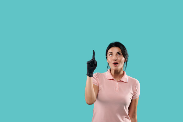 年轻女子惊讶地抬起头，用食指指着上面。孤立的肖像在蓝色背景与复制空间图片下载