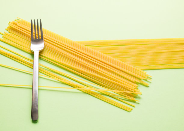 创意的背景由生意大利面组成的绿色背景，两层意大利面随机放置与钢叉。图片下载