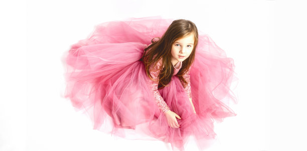 小公主。一个可爱的白人小女孩的肖像在一个晚上亮粉色的裙子坐在白色的背景。水平。图片下载